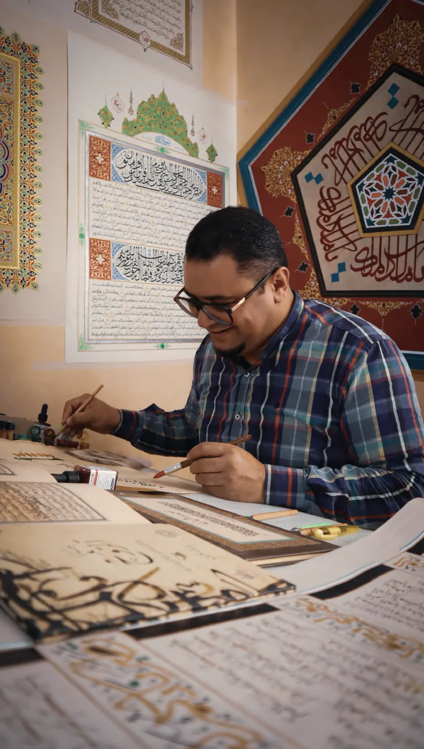 الأستاذ محمد أمين بوحيد يكتب في مرسمه بين أدوات الخط